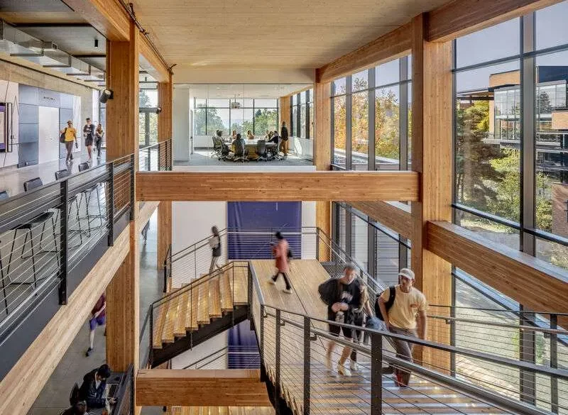 The timber and glass atrium of Founders Hall, with students on the stairs and glazed meeting rooms above.