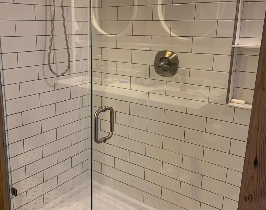 Frameless glass shower door in a white tile bathroom