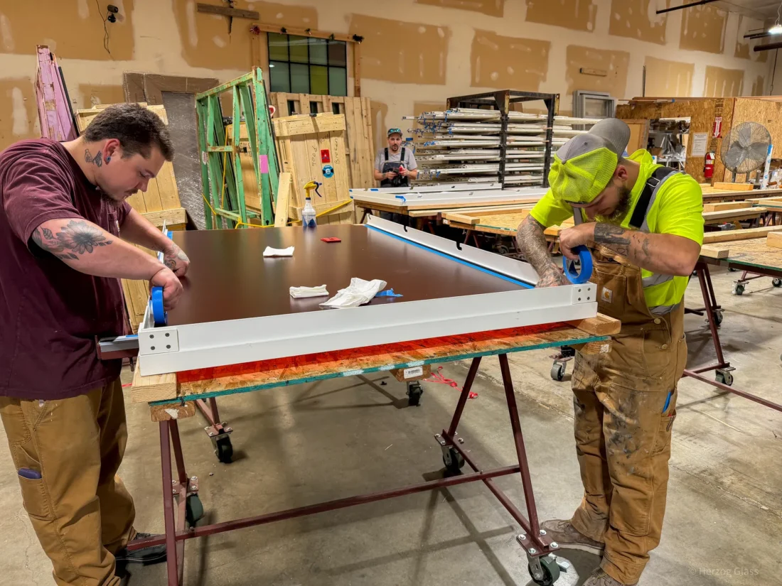 Aluminum and glass canopy assemblies and their shop drawings on the fabrication floor.