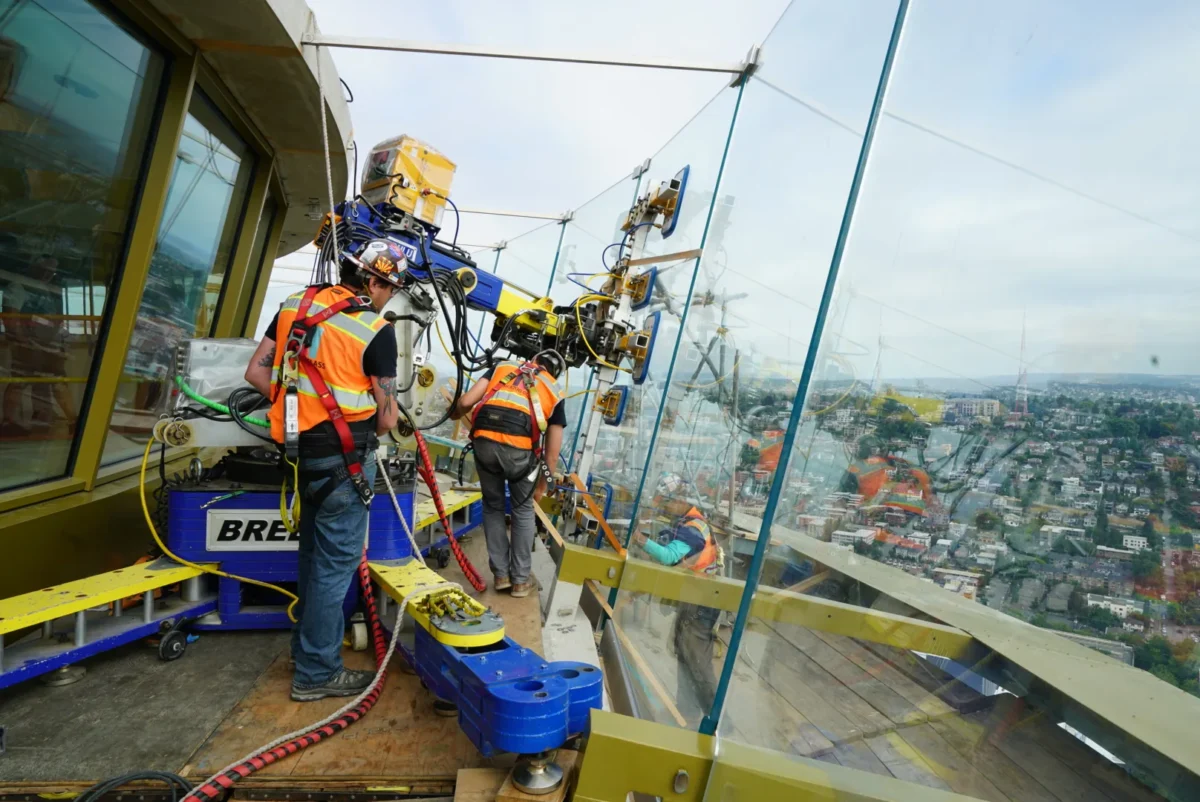 Two glaziers setting a curved observation deck panel with a vacuum lifter