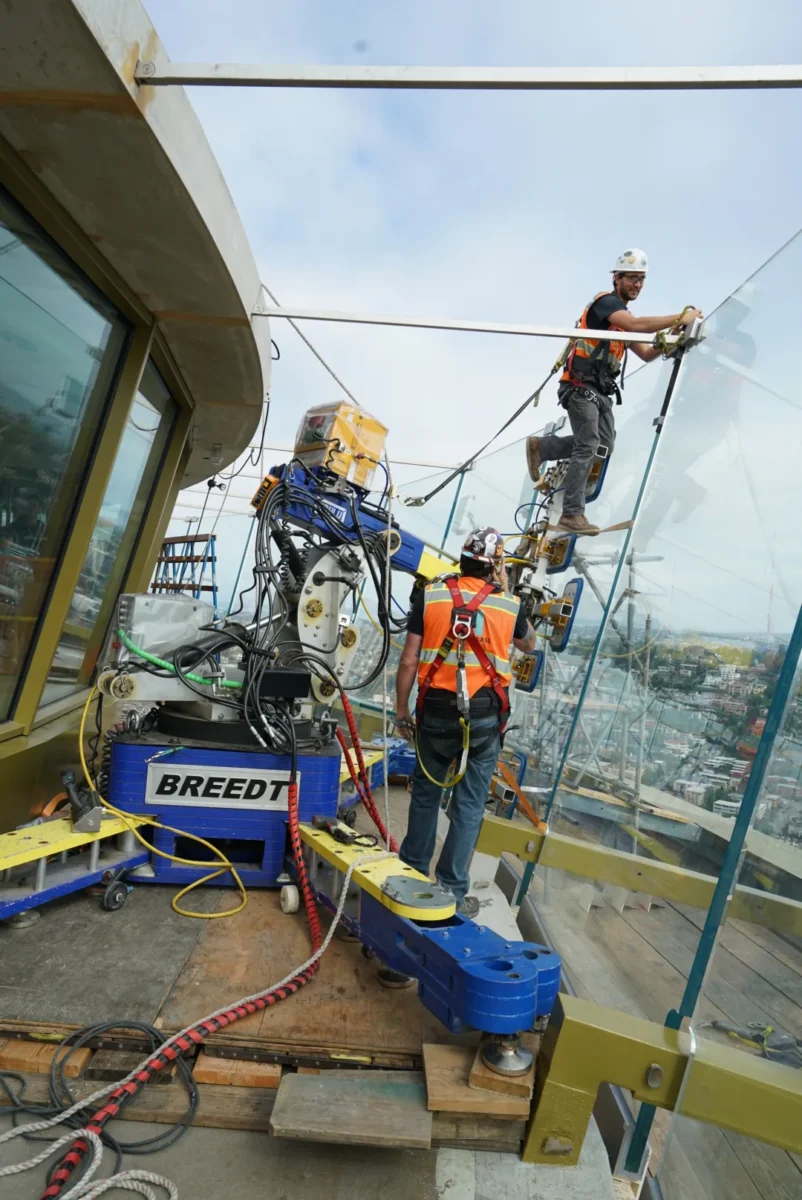 A glazier in a harness guiding a new glass panel into the observation deck frame