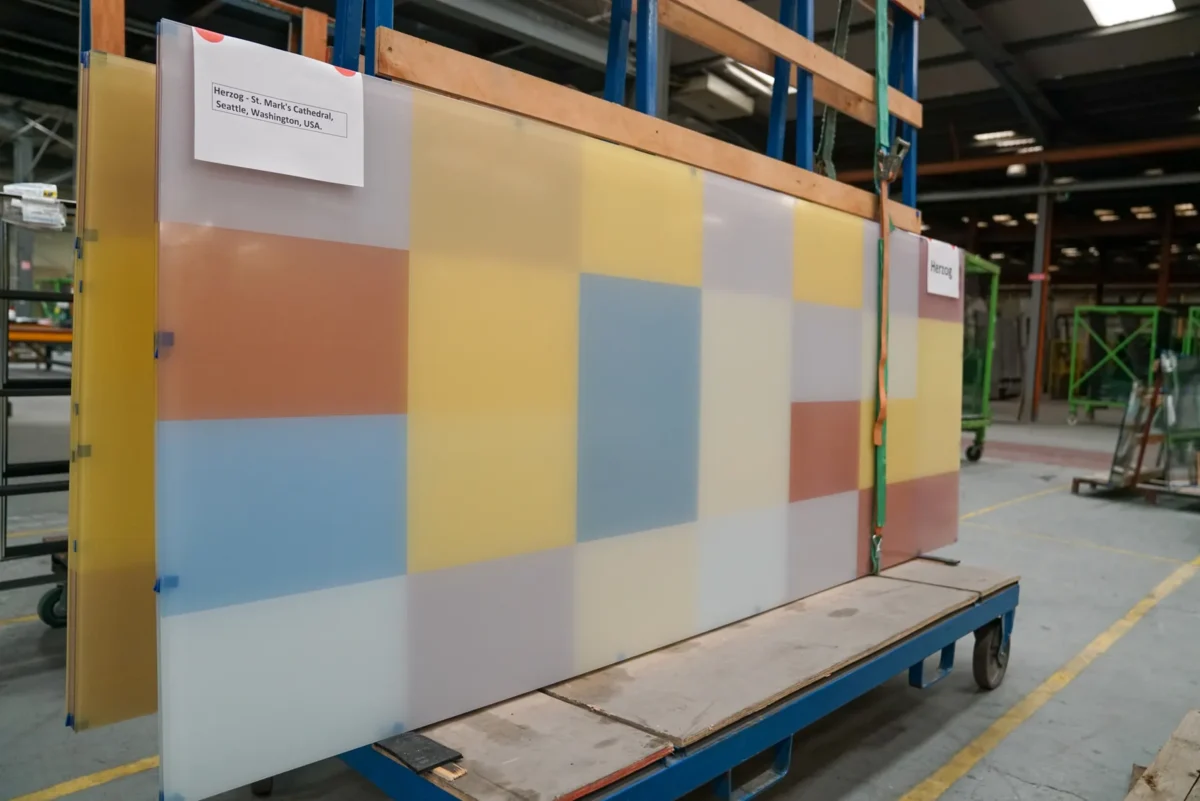 Colored glass panels in the arched windows of St Mark’s Cathedral, and the same panels on the shop floor before installation.