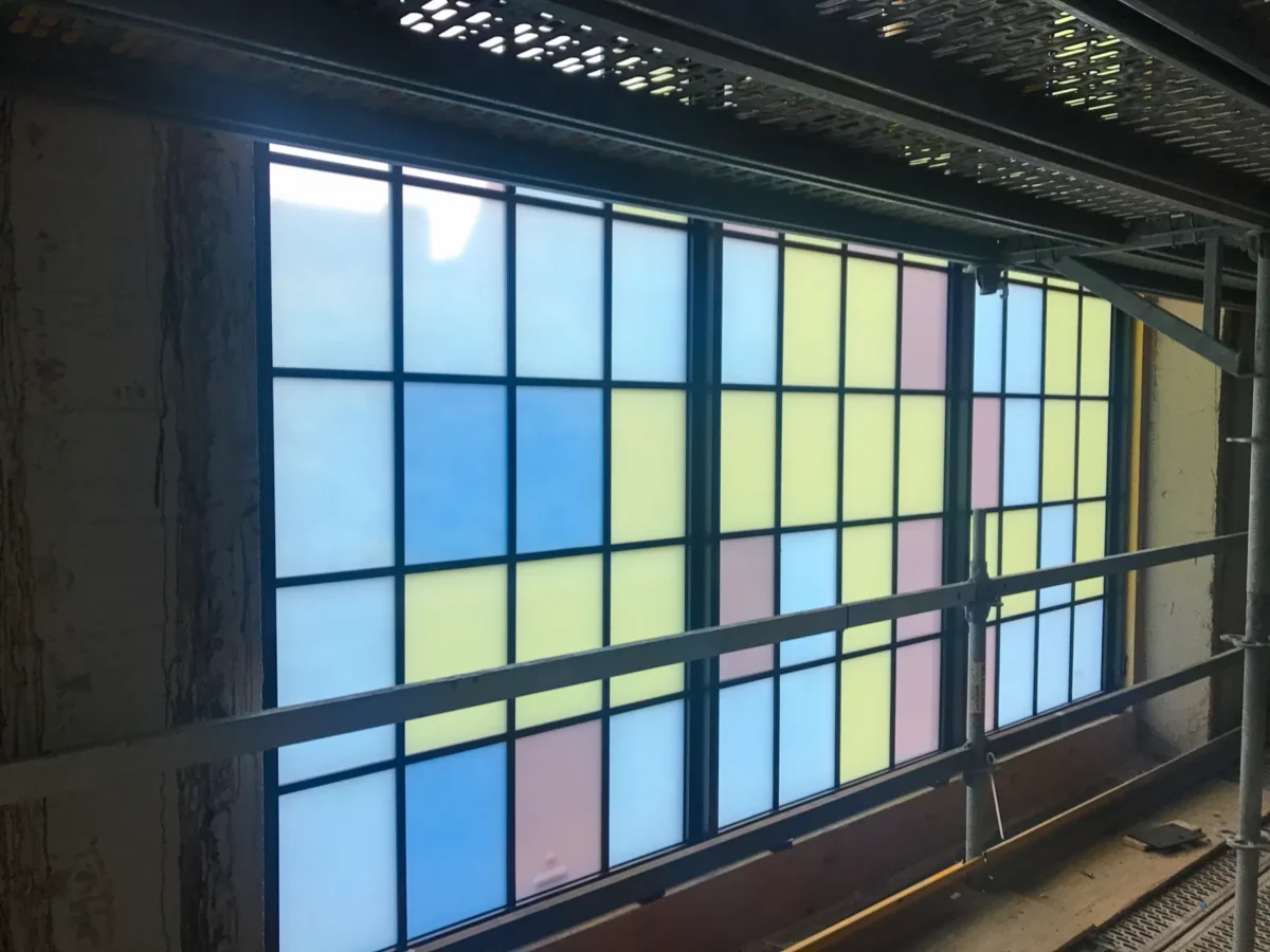 Colored glass panels in the arched windows of St Mark’s Cathedral, and the same panels on the shop floor before installation.